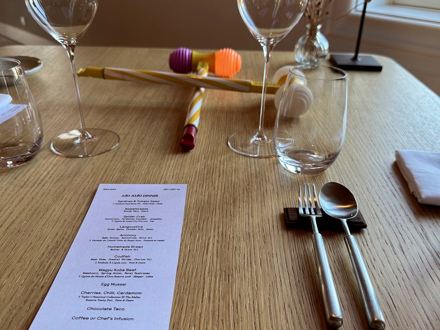 Two plastic São João hammers on a São João dinner table at WOW, beside the menu